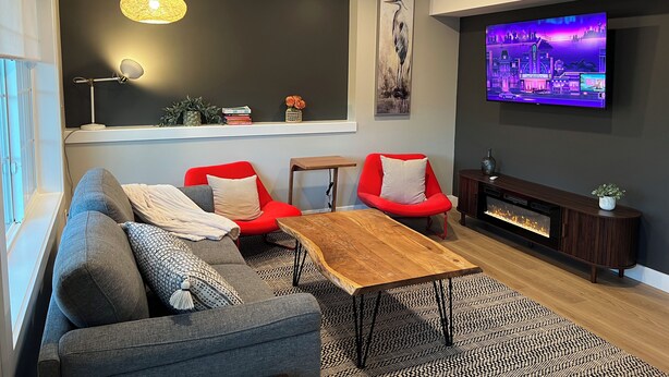 Un salon moderne avec un canapé gris, des fauteuils rouges, une table basse en bois, un téléviseur et une cheminée.