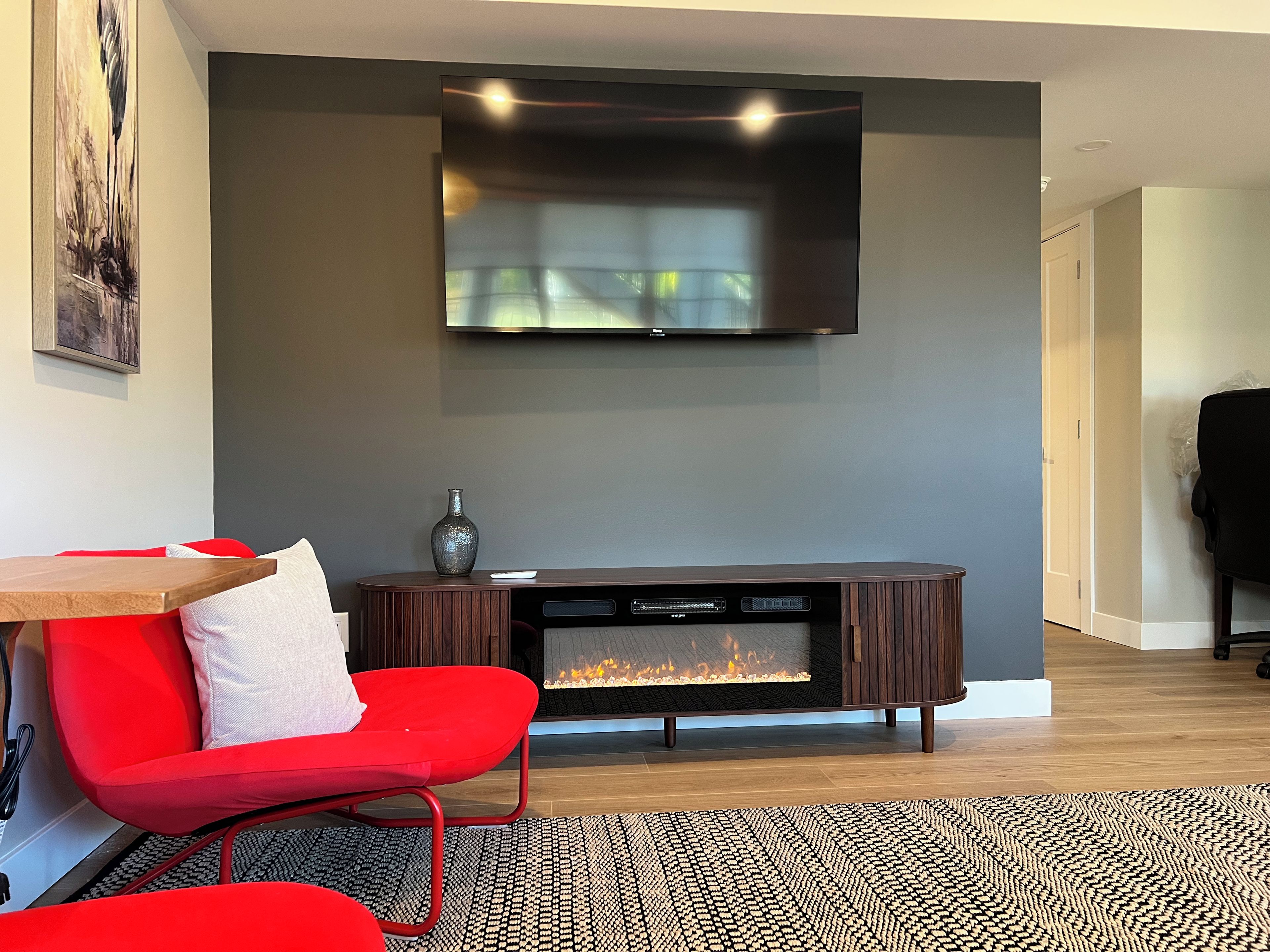 Una sala moderna con un televisor de pantalla plana montado en la pared, una chimenea, un sillón rojo y una mesa de centro de madera.