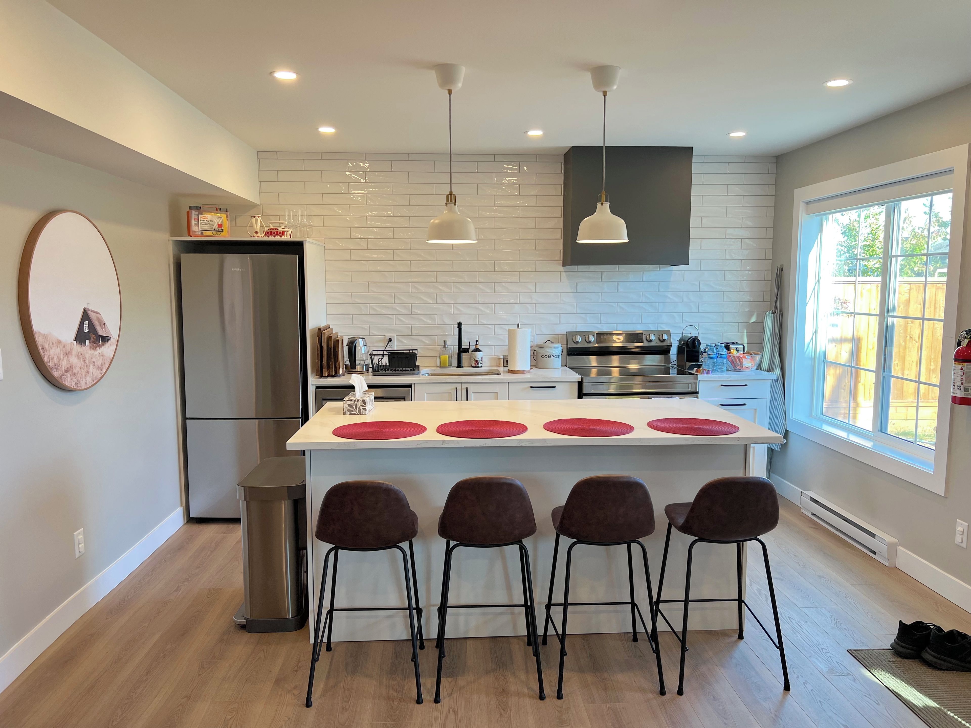 A modern kitchen with a central island, bar stools, and a large window.