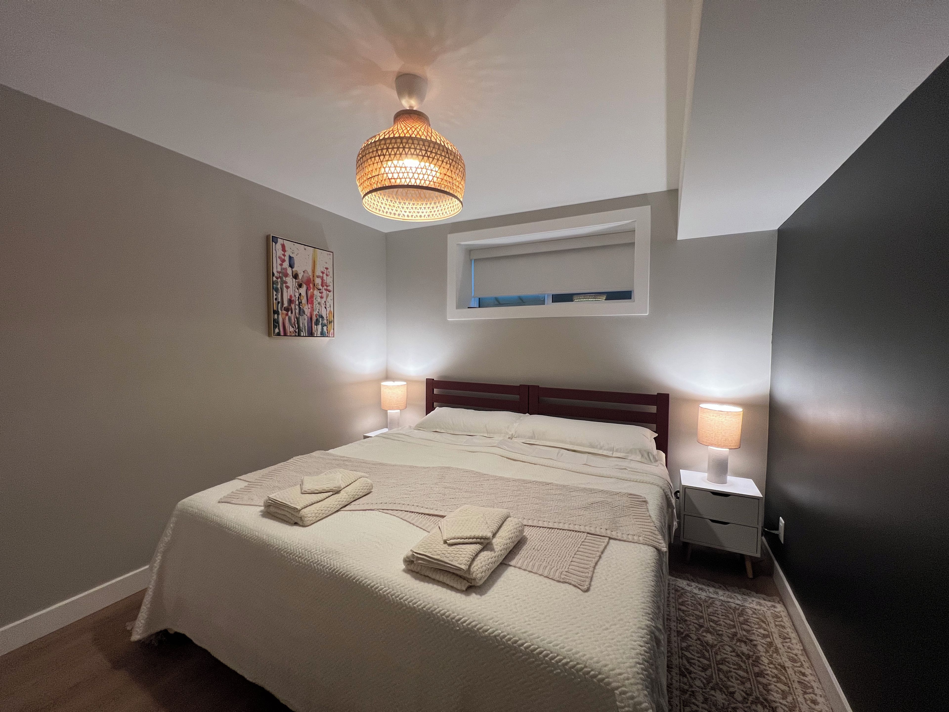 Un dormitorio con una cama grande, dos lámparas de noche, una lámpara de techo, una obra de arte enmarcada y un estante empotrado sobre la cama.