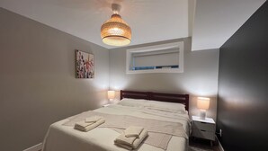 Une chambre à coucher avec un grand lit, deux lampes de chevet, un luminaire au plafond, un tableau encadré et une étagère intégrée au-dessus du lit.