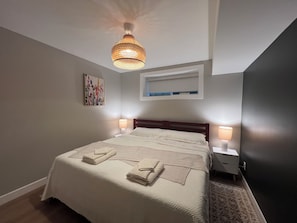Un dormitorio con una cama grande, dos lámparas de noche, una lámpara de techo, una obra de arte enmarcada y un estante empotrado sobre la cama.
