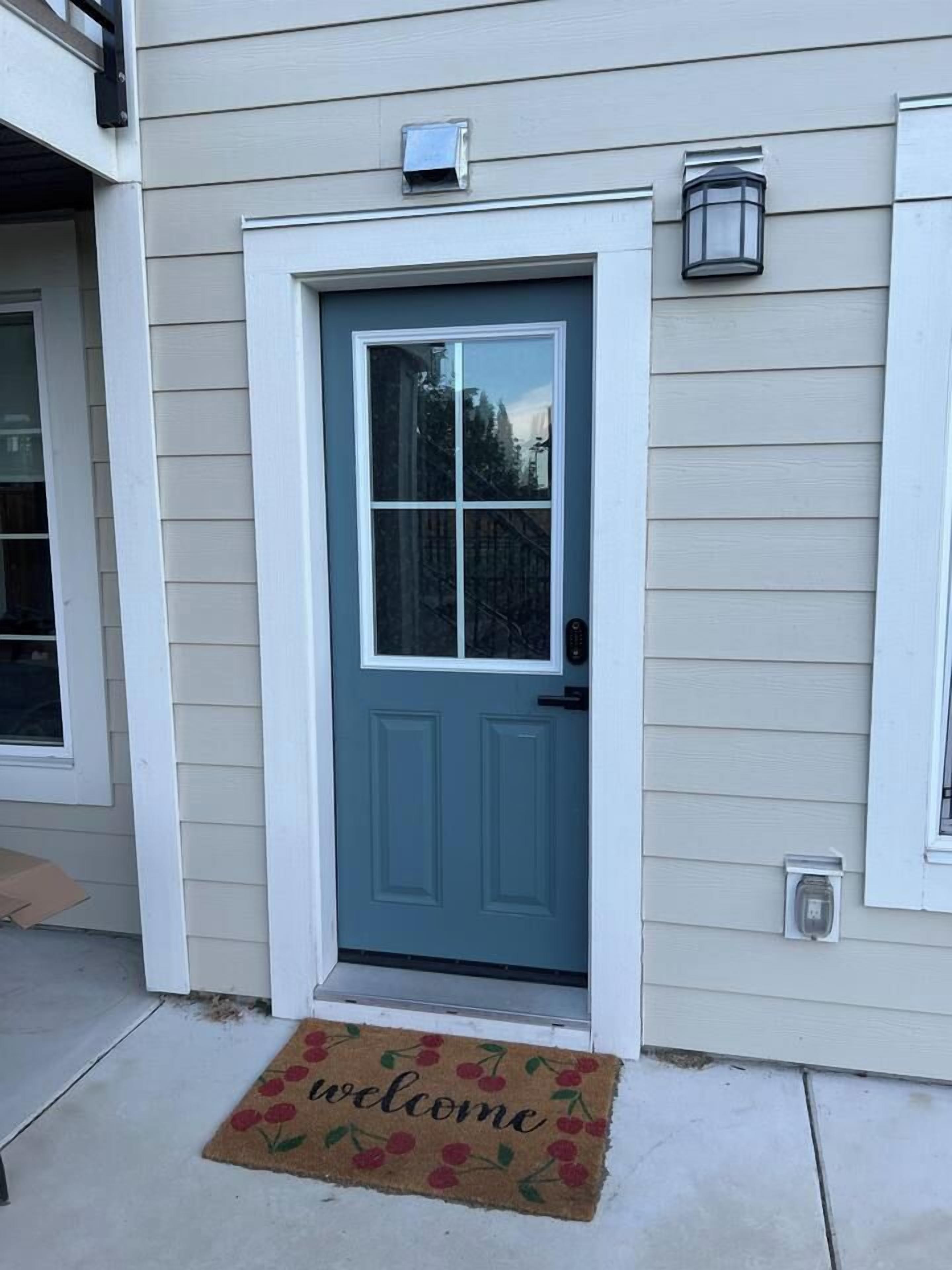 A front door with a welcome mat, a mailbox, and a wall-mounted light fixture.