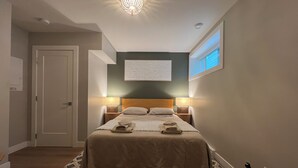Une chambre d’hôtel avec un lit, deux lampes de chevet, une œuvre d’art accrochée au mur et une fenêtre avec des stores.