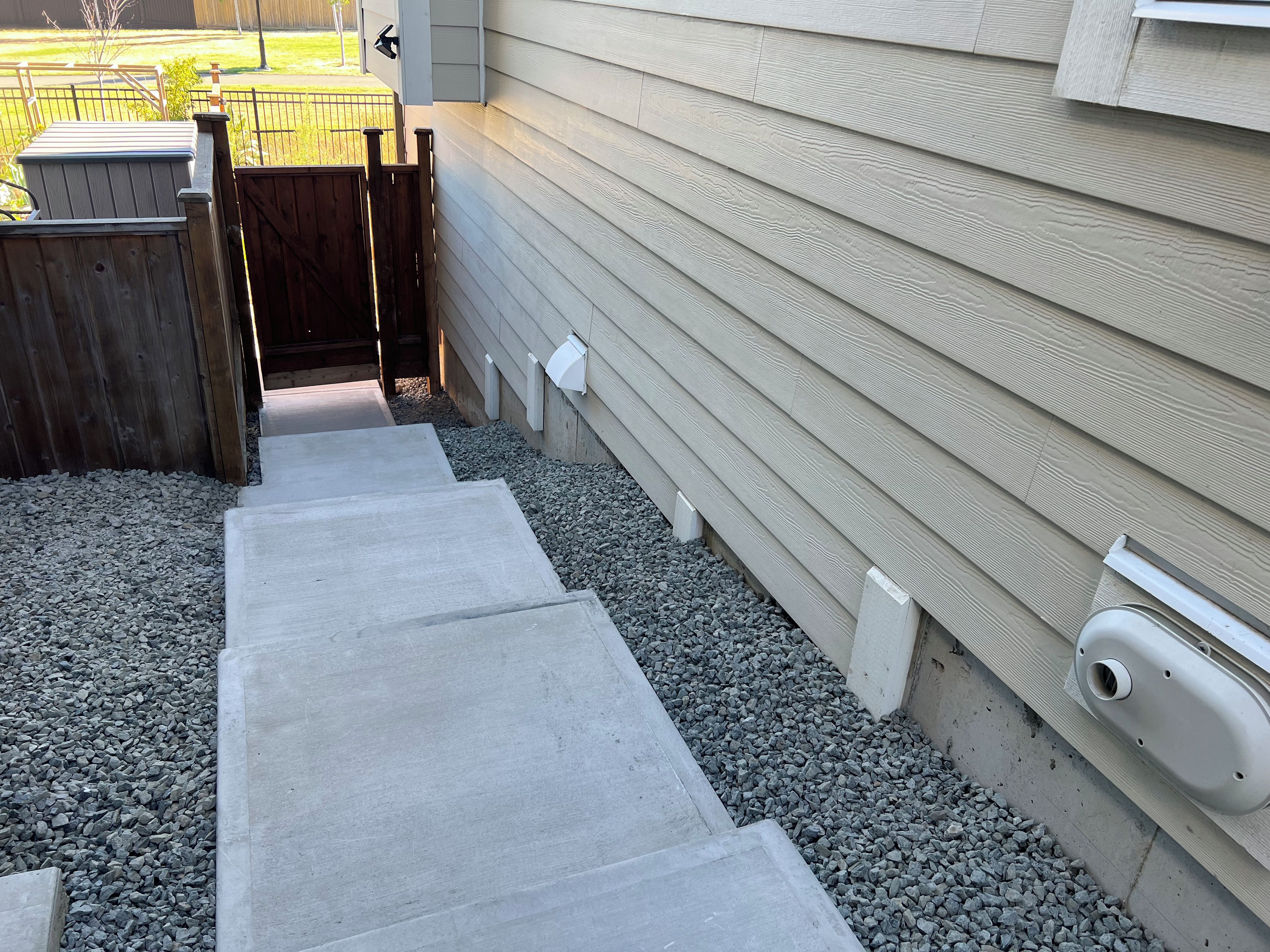 Ein Betonweg führt zu einem Holztor, mit einem Kiesbereich und einem Haus mit Schalung.