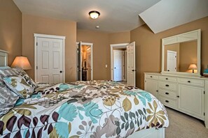 Quarto com cama, penteadeira, espelho e porta que dá para outro cômodo.