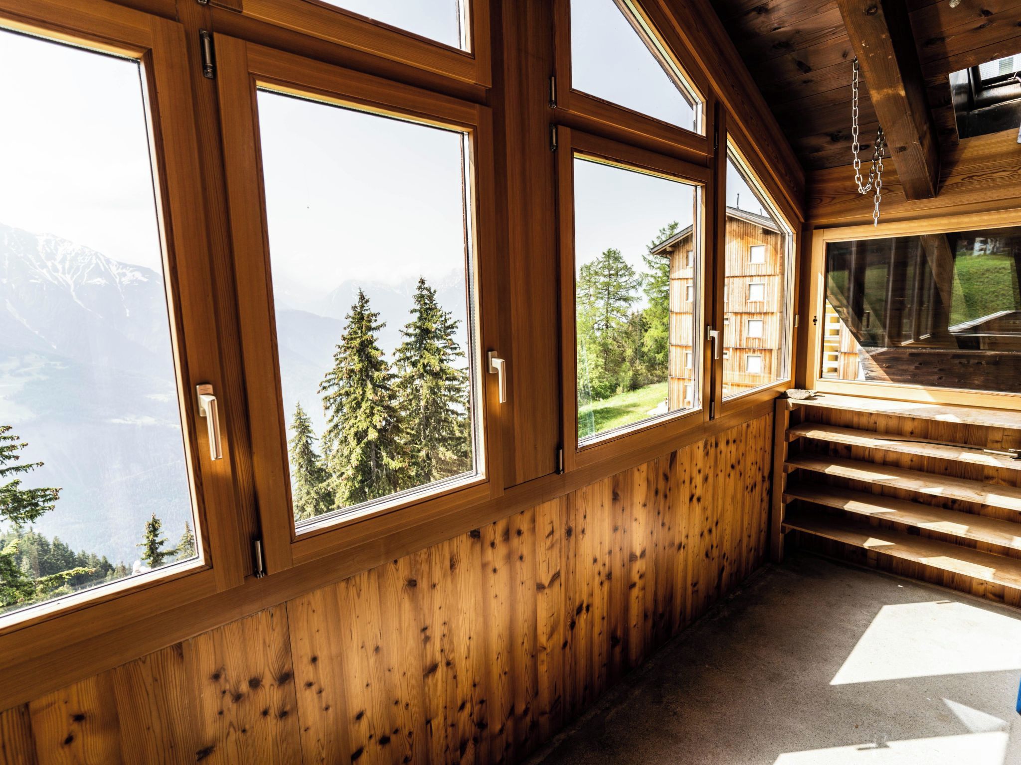 Una habitación con ventanas amplias, paredes de madera y vistas a montañas y árboles.