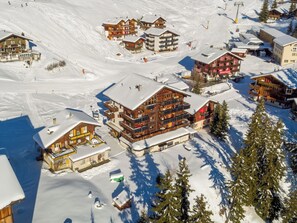 Une station de montagne enneigée, avec de nombreux bâtiments en bois, des remontées mécaniques et un ciel dégagé.