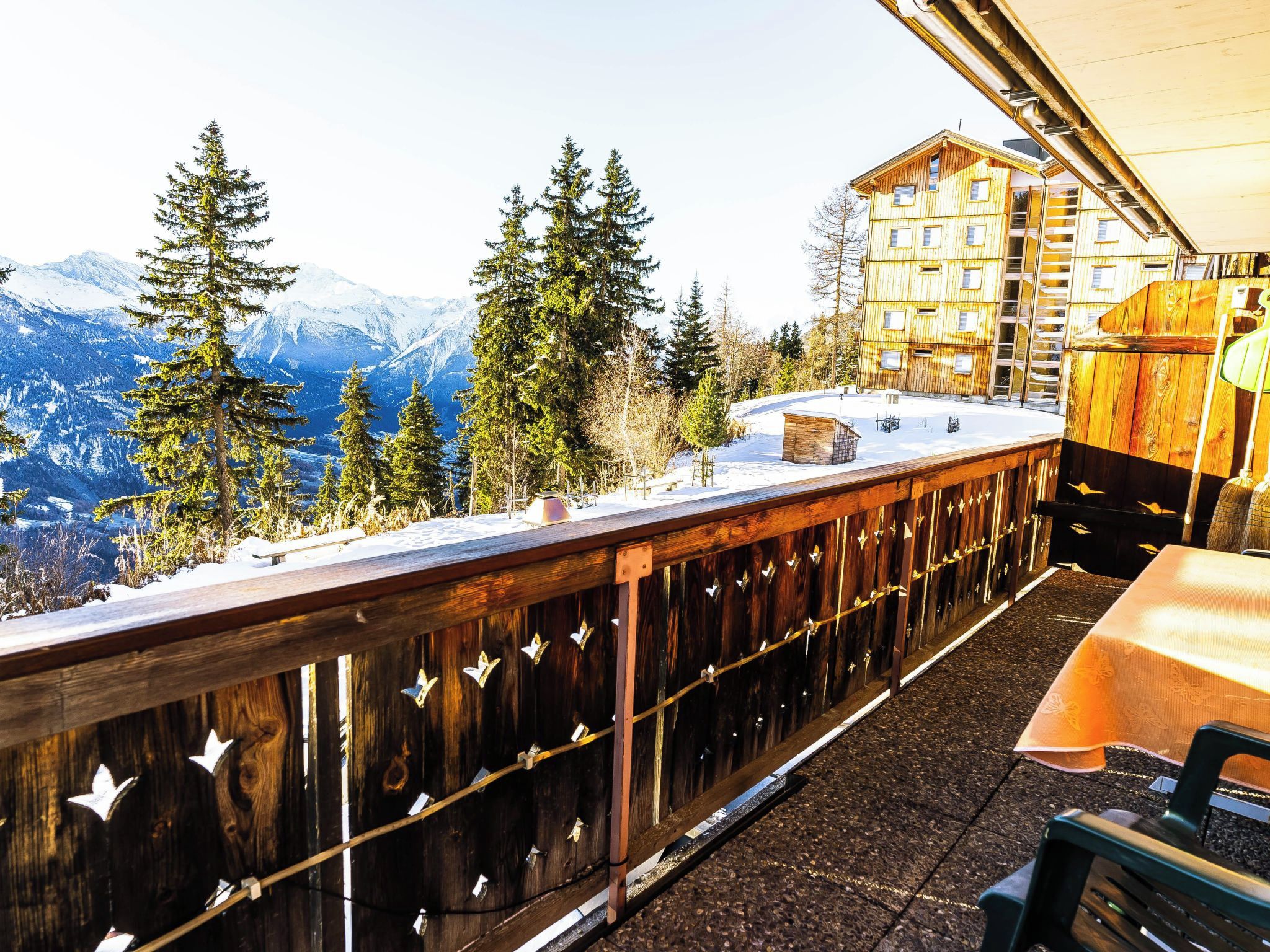 Una terraza de madera con vistas a montañas nevadas y un edificio al fondo.