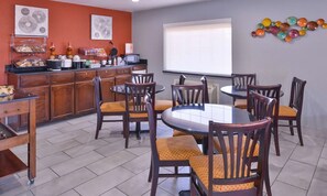 Un comedor con una mesa redonda y sillas, una encimera de cocina con varios objetos, y obras de arte en las paredes.