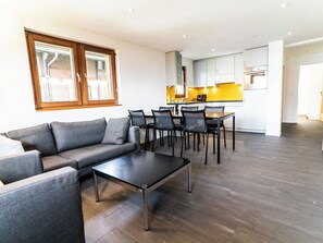 En moderne stue med en grå sofa, et sort sofabord og et spiseområde med stole og et bord.