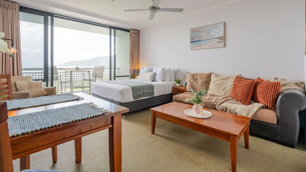 Habitación de hotel con cama, sofá, mesa de centro y balcón con vistas.