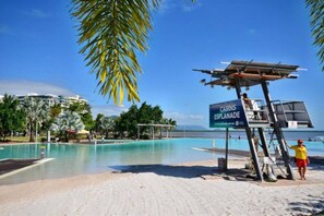 A beach with a lifeguard tower, a sign for Cairns Esplanade, and a pool area. - Rydges 92B | 9th Floor City & Esplanade Views (Cairns North)