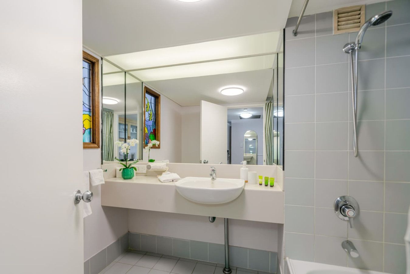 A modern bathroom with a large mirror, a sink, and a shower.