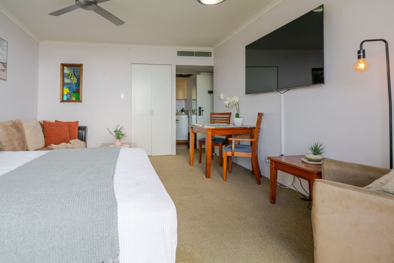 A hotel room with a bed, a desk, a chair, a sofa, a dining table, and a TV.