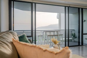 En moderne stue med en sofa, et lille bord med en vase og en balkon med en hvid stol og en potteplante.