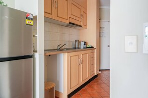 A kitchen with a stainless steel refrigerator, wooden cabinets, a tiled backsplash, and a sink. - Cozy Budget 1BR in Cairns City with Pool (Cairns City)