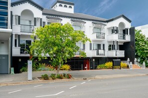 A multi-story building with balconies, a tree in the foreground, and a clear sky. - Cozy Budget 1BR in Cairns City with Pool (Cairns City)