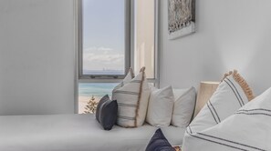 Ein Bett mit Kissen und Blick auf den Strand durch ein Fenster.