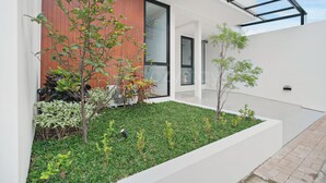 Un edificio moderno con facciata in vetro, un piccolo giardino con diverse piante e un vialetto in mattoni.