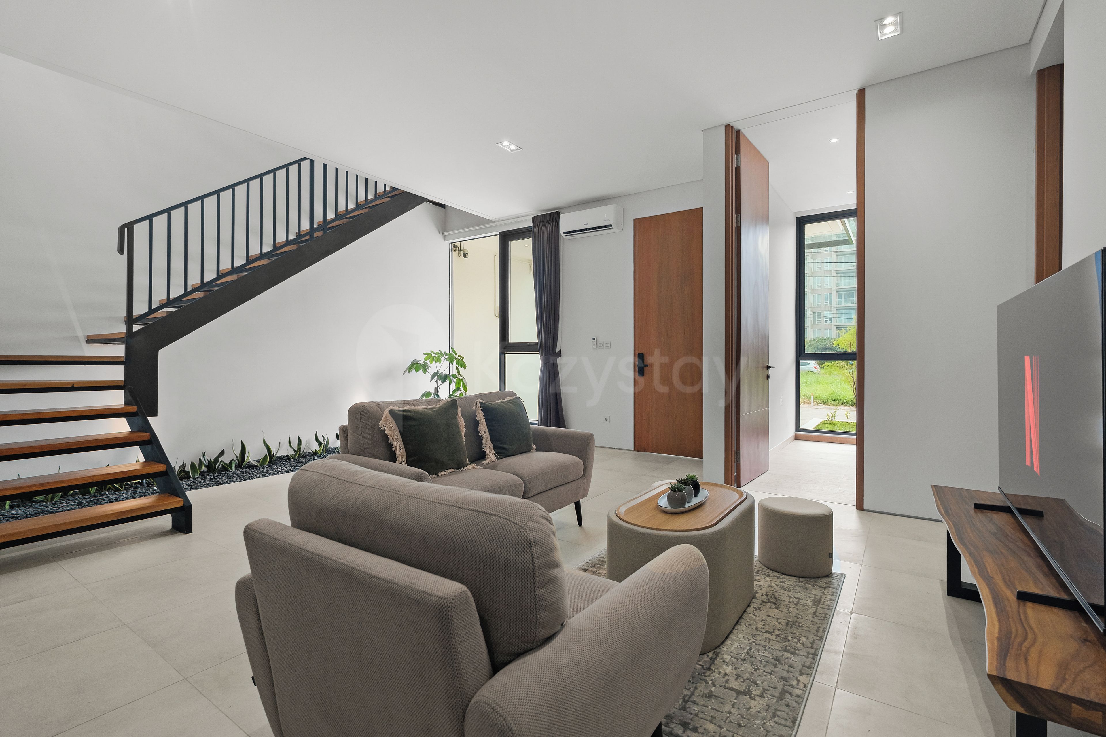 Una sala de estar moderna con una escalera, zona de estar y televisor.