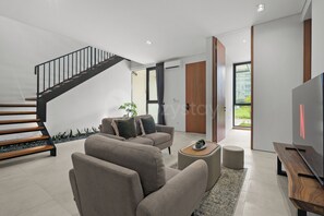 A modern living room with a staircase, seating area, and a television. - Anaya Villa by Kozystay - Paskal (Bandung)