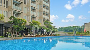 Una piscina con lettini e sdraio, con un edificio e balconi sullo sfondo.