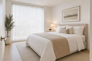 Un dormitorio con una cama, una mesita de noche con lámpara, una planta en maceta y una ventana con persianas.