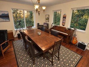 A dining area with a wooden table, chairs, a piano, a guitar, and a tripod-mounted camera. - Private Mission Lake retreat: hot tub, dock, paddleboards & record player (Bremerton)