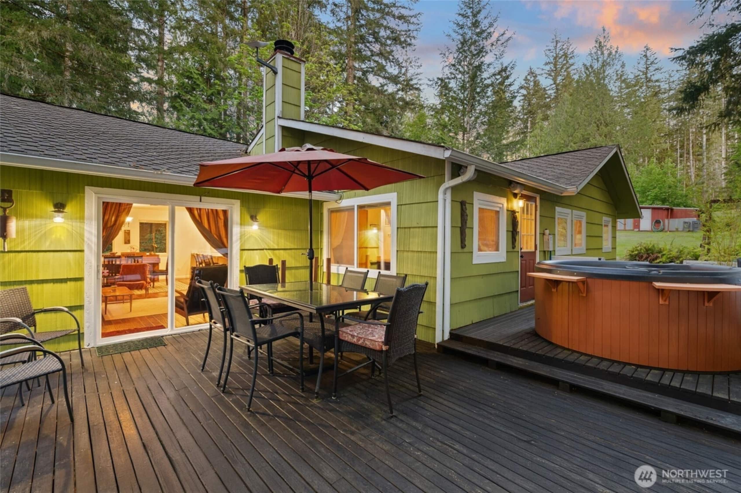 A wooden deck with a glass-top table and chairs, a hot tub, and a covered patio area.