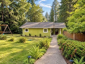 A single-story house with a green exterior, a front porch, and a pathway leading to the entrance. - Private Mission Lake retreat: hot tub, dock, paddleboards & record player (Bremerton)