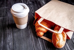 Una taza de café y una bolsa de papel con pan sobre una superficie de madera.