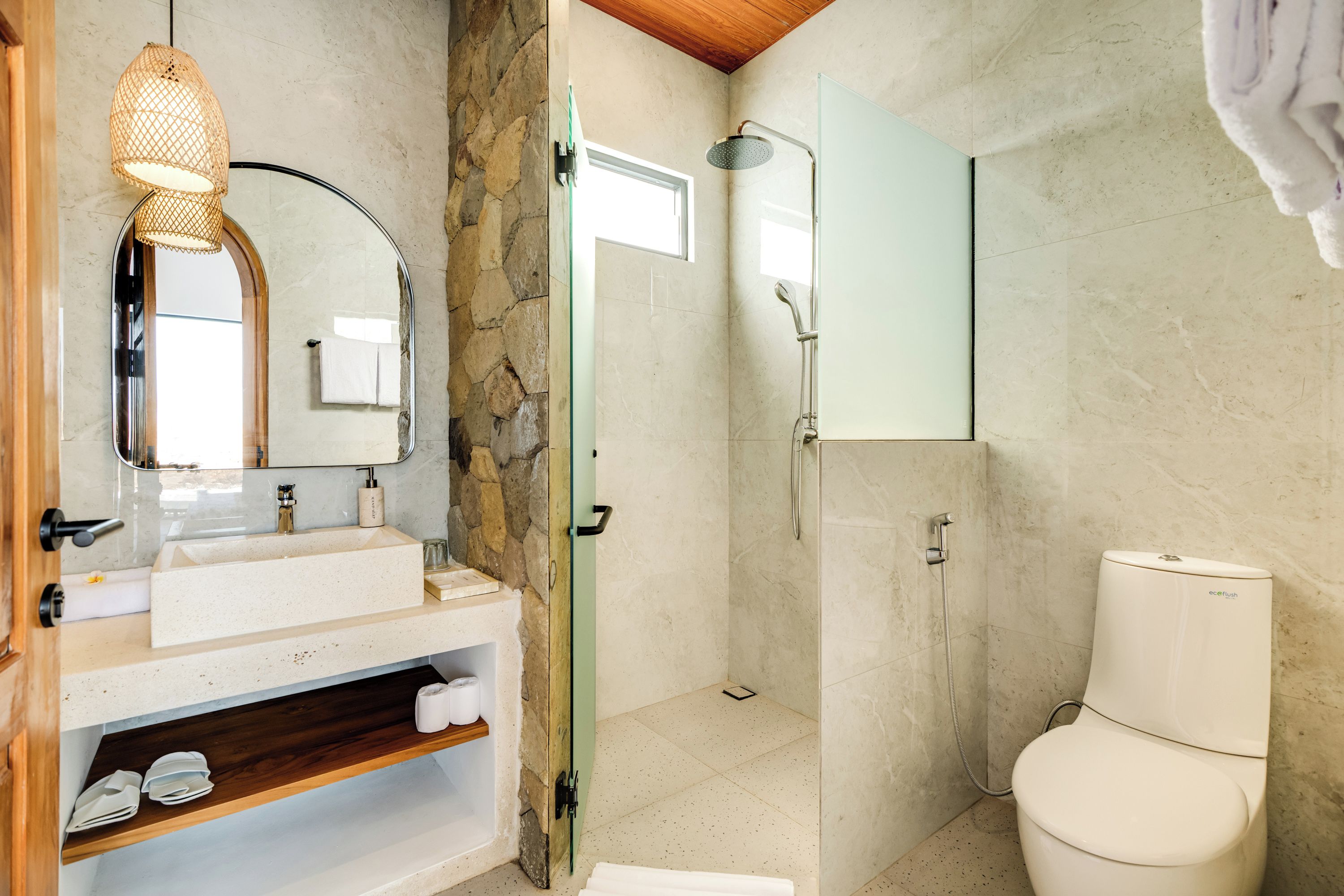 A bathroom with a stone wall, a sink with a mirror, a shower with a handheld showerhead, and a toilet.