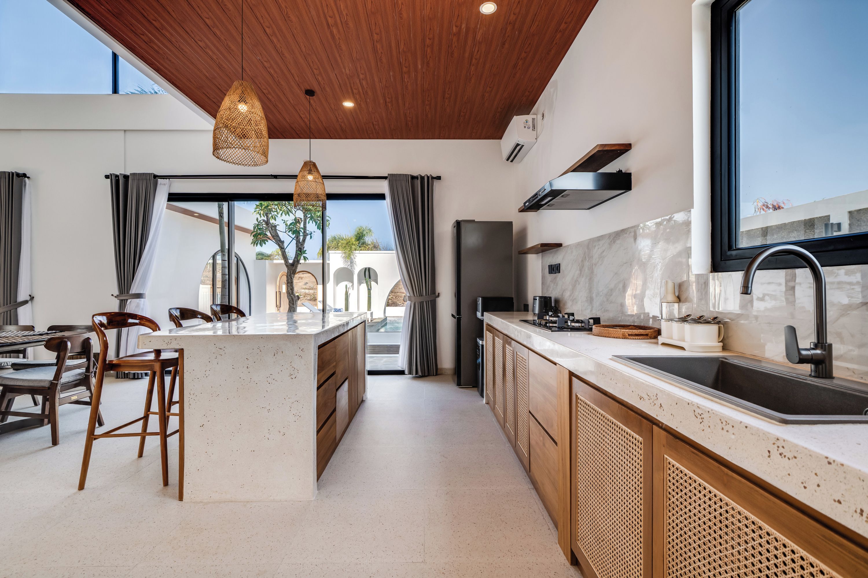 Una cocina moderna con una isla central, armarios de madera, un lavamanos de acero inoxidable y vistas al exterior.