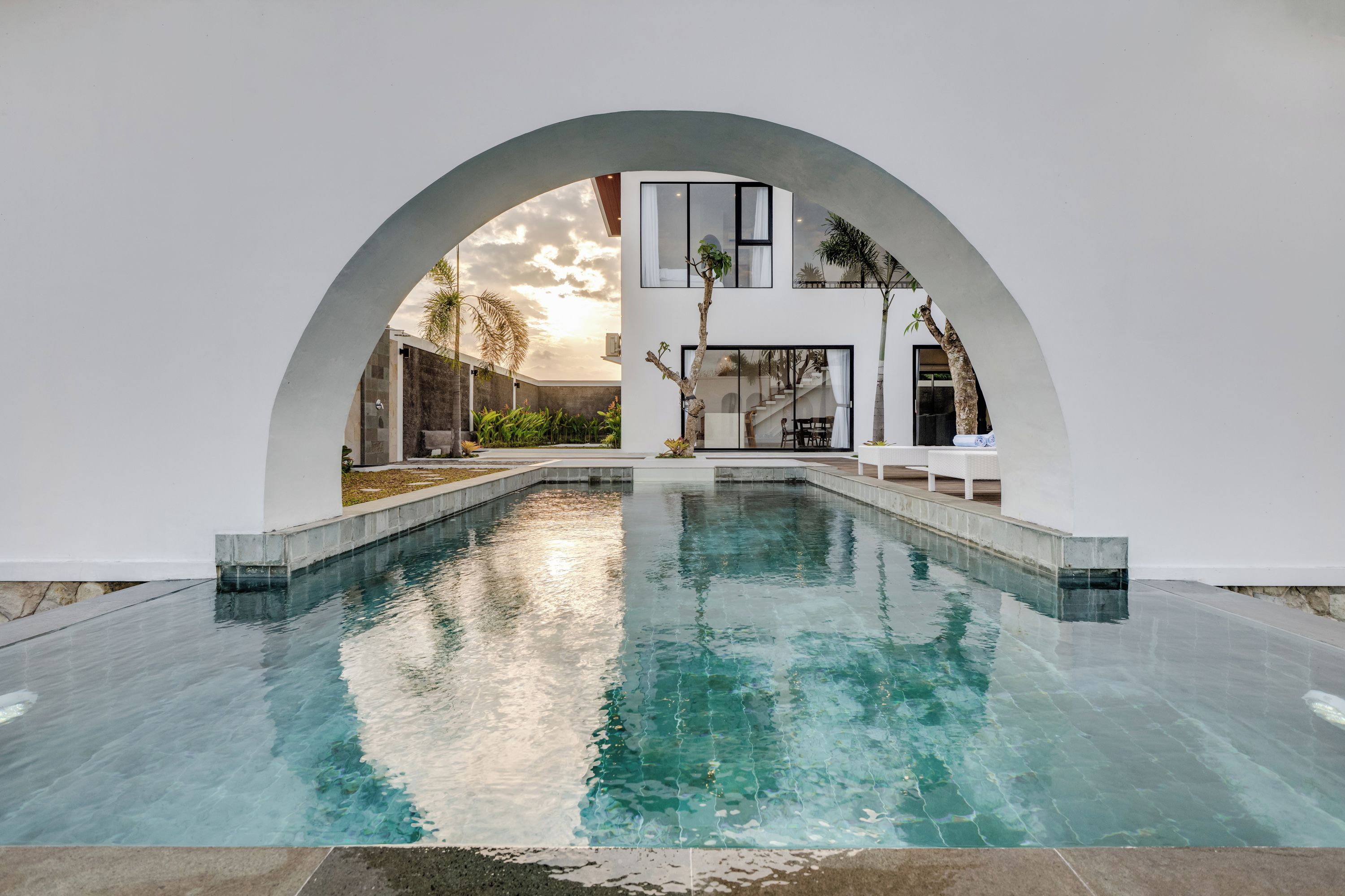 A modern pool area with a clear water surface, surrounded by white walls and an arched structure.
