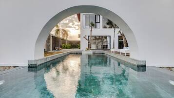 A modern pool area with a clear water surface, surrounded by white walls and an arched structure.