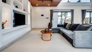A modern living room with a flat-screen TV, a sofa, a coffee table, and a large window.