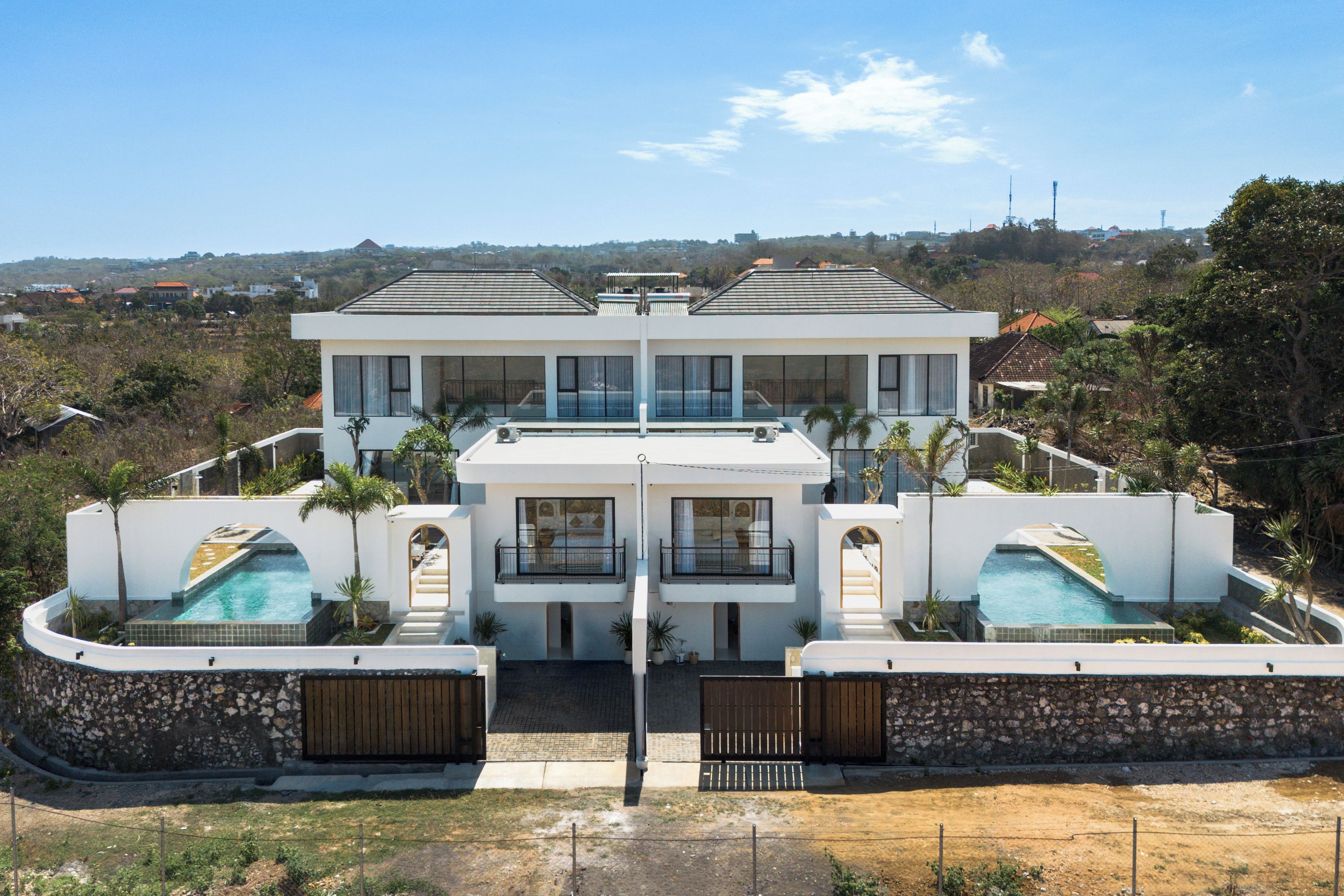 A large, modern two-story house with a swimming pool, a stone wall, and a view of the surrounding landscape.