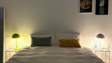 A neatly made bed with two pillows, a bedside table with a lamp, and two wall-mounted artworks.
