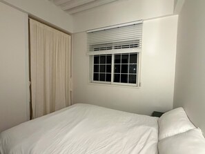 Un dormitorio con una cama, una ventana con persianas y una puerta.