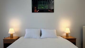 Una habitación de hotel con una cama, dos lámparas de noche, un cuadro en la pared y una mesita de noche.