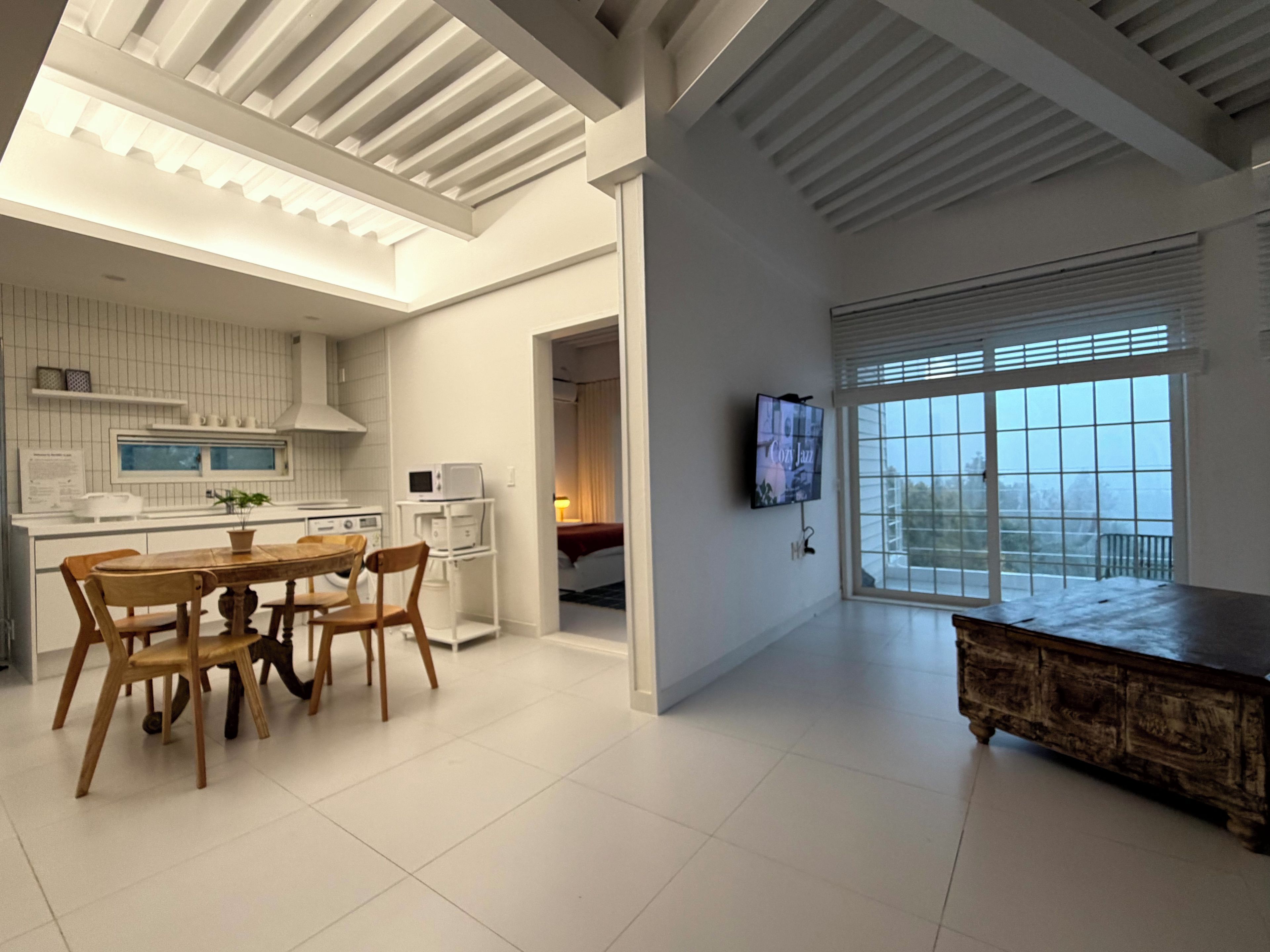 A modern interior with a dining area, kitchen, and a large window with blinds.