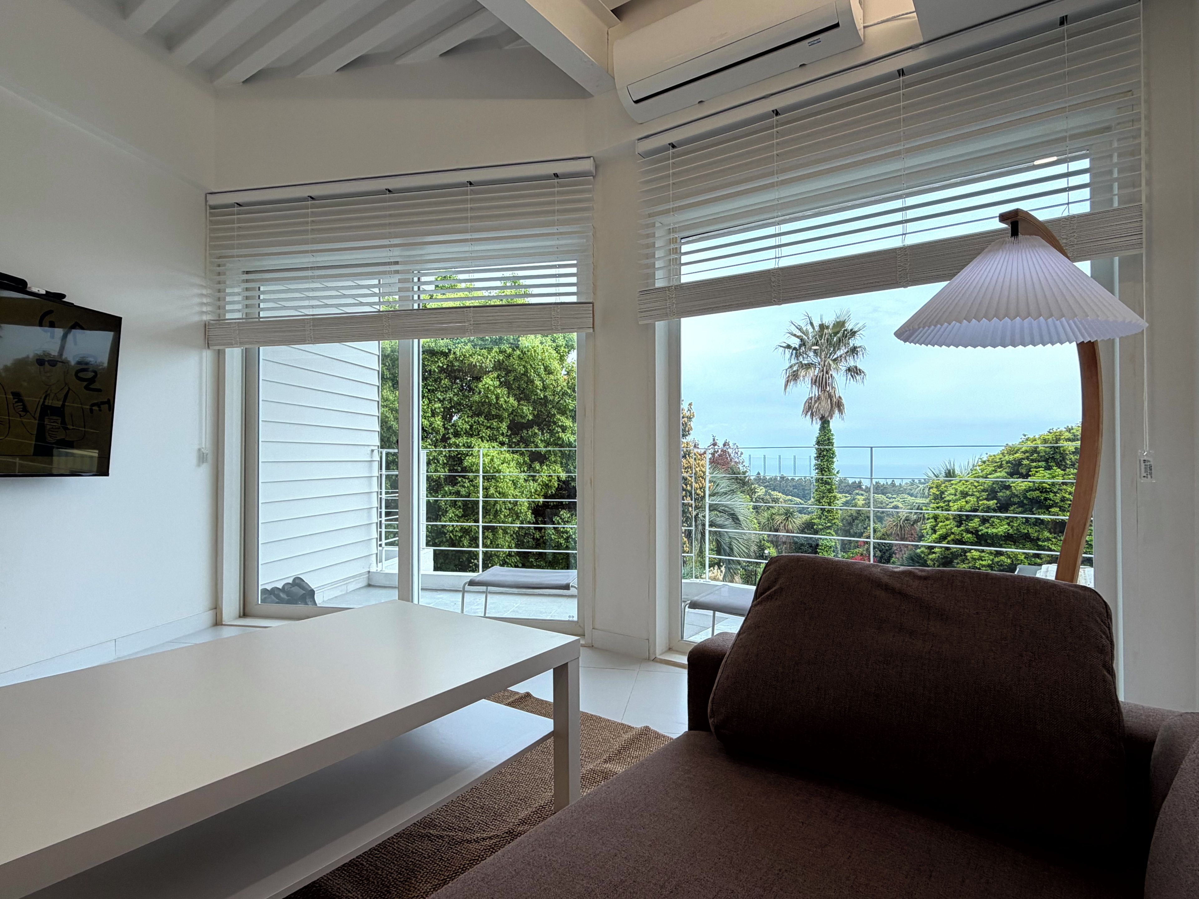 A modern room with a white table, a brown sofa, and large windows with blinds.