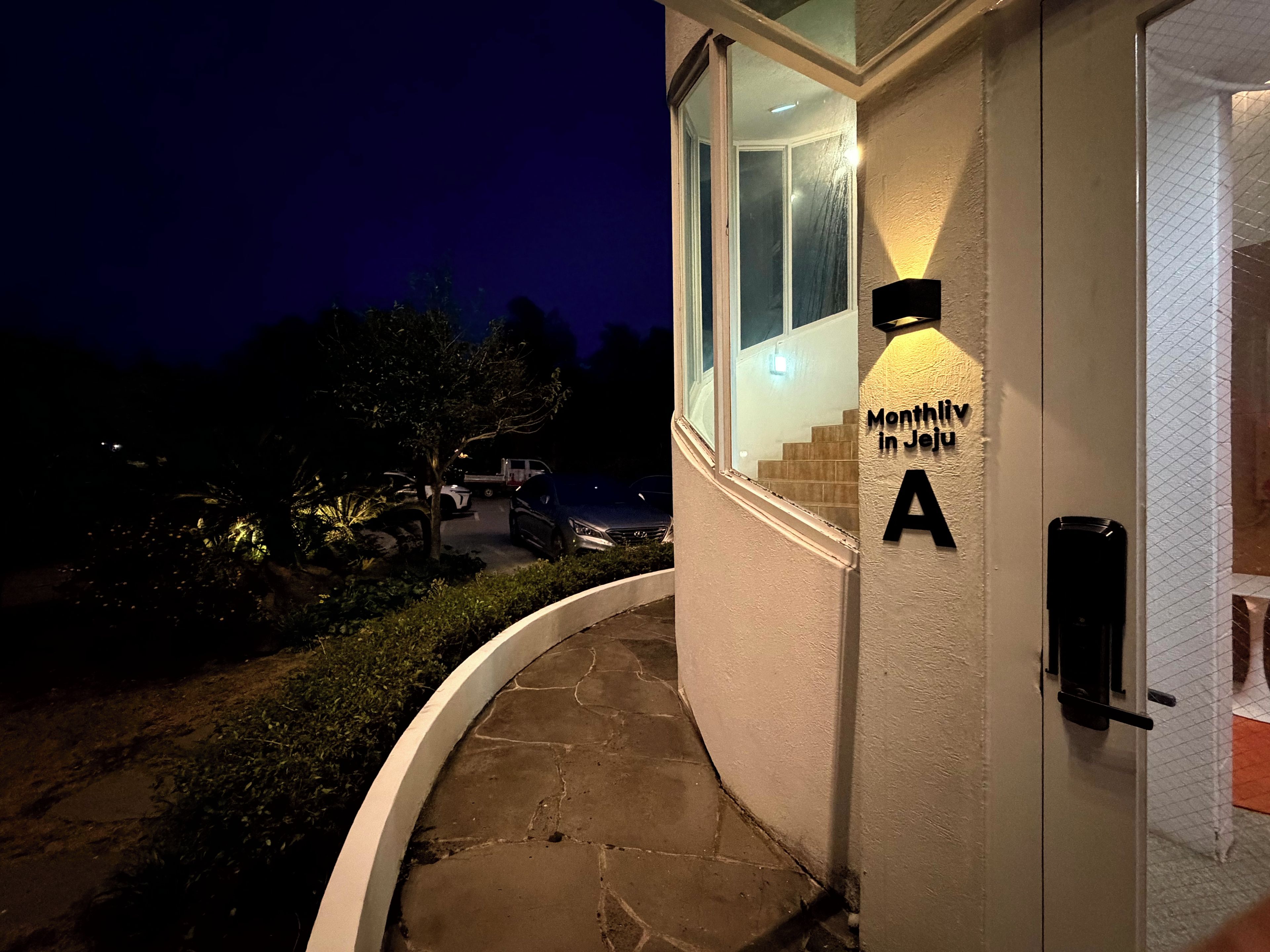 A building entrance with a sign reading 'Monthly in Jeju A' and a door with a keypad lock.