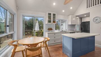 A modern kitchen with a central island, white cabinetry, and a dining area with wooden chairs.