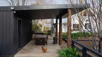 A covered outdoor area with a table and chairs, a chicken, and a garden.