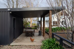 Un espacio al aire libre techado con una mesa, sillas, una gallina y un jardín.