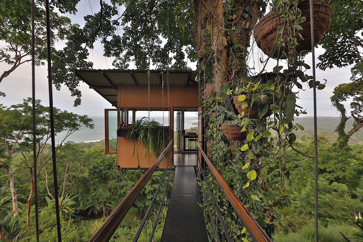 Ein Baumhaus mit Holzfassade, einer Metalltreppe und Blick auf den Ozean.