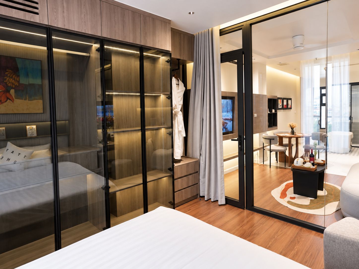 A modern hotel room with a bed, a seating area, a television, and a glass partition.