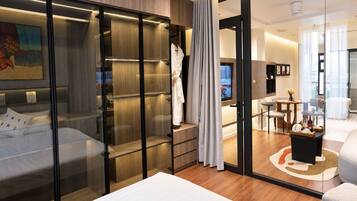 A modern hotel room with a bed, a seating area, a television, and a glass partition.